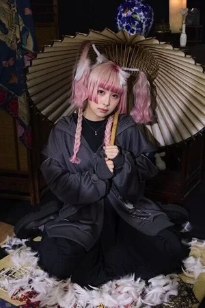 黒いフード付きジャケットを着て、和傘を背に羽根の中に座るモデル