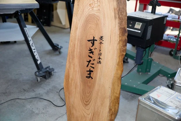 天然木の耳付き一枚板に『煮干しと日本酒 すぎだま』と墨文字で書かれた店舗看板
