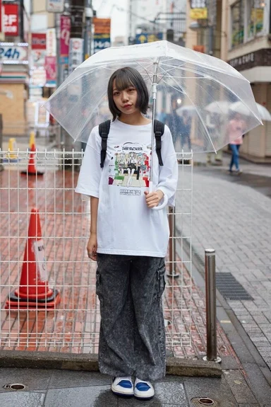 雨の街角で傘をさすモデル。イラストをプリントした白のTシャツ