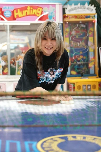 ゲームセンターのエアホッケー台に向かうモデル。キャラクターをプリントした黒のTシャツ