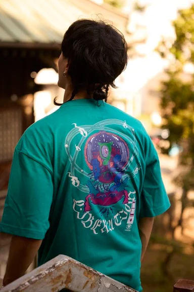 緑のTシャツの後ろ姿。背中いっぱいに多色のイラストがプリントされている