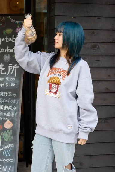 直売所の前に立つモデル。フライドポテトのイラストをプリントしたグレーのトレーナー