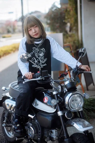 バイクにまたがるモデル。キャラクターをプリントした黒Tシャツを白の長袖に重ねている