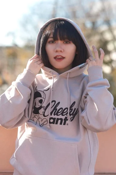 フードをかぶるモデル。Cheeky antのロゴとキャラクターが入ったベージュのパーカー