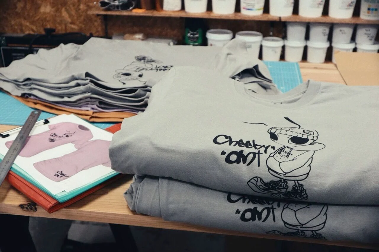 Cheeky antのプリントを終えて畳まれたTシャツと、指示書を置いた作業台