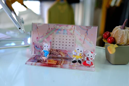 パステルカラーの背景にカレンダーが入ったアクリルスタンド。手前に、小さなアップちゃんのアクリルパーツが3つ立っている