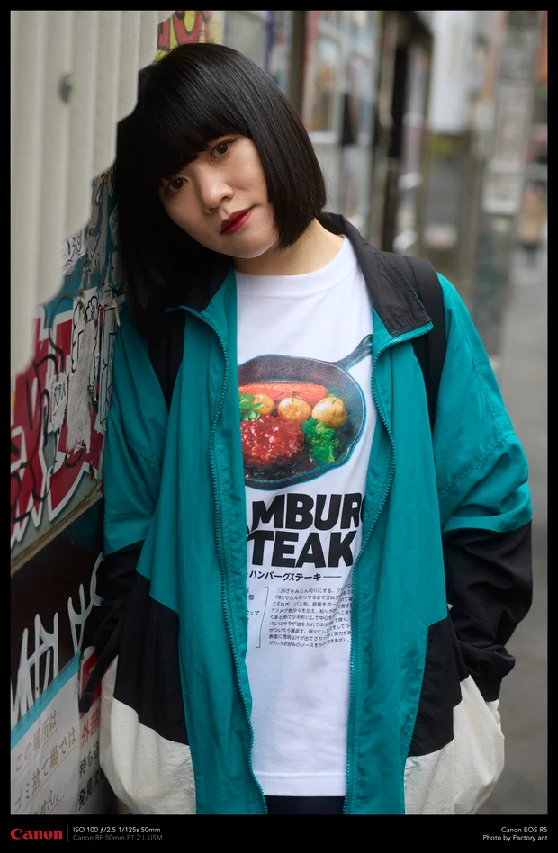 緑のジャージを羽織ったモデル。Cheeky ant のハンバーグステーキのイラスト入り白Tシャツ