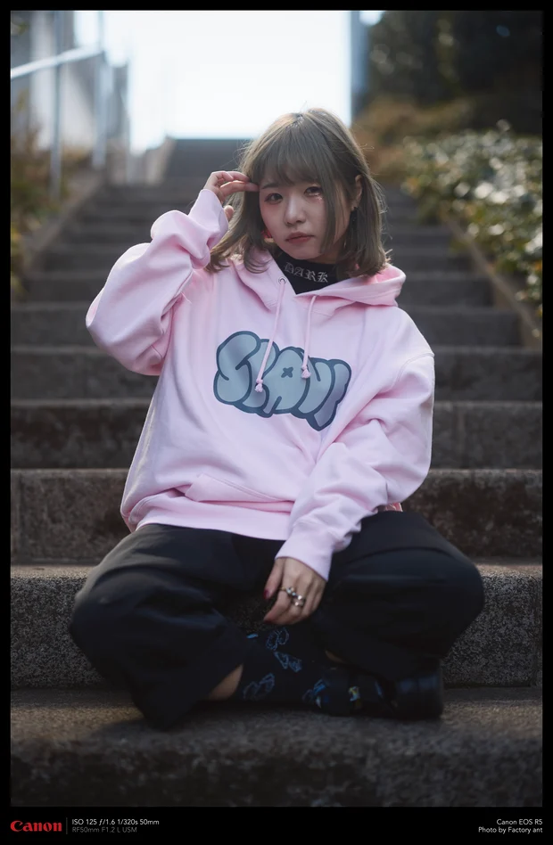 階段に座るモデル。Kawaii Apparel のロゴ入りピンクのパーカー