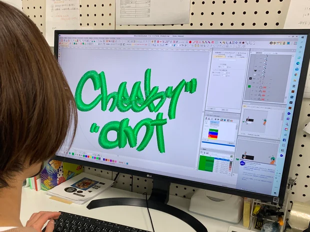 スタッフが刺繍データ作成ソフトの画面で、「Cheeky ant」のロゴを緑色の糸の刺繍データに仕上げている様子