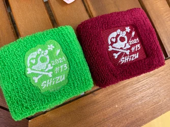 緑とえんじ色のパイル地のリストバンドに、白い糸でドクロと骨の図柄と「2021 #13 SHiZU」の文字を刺繍したもの