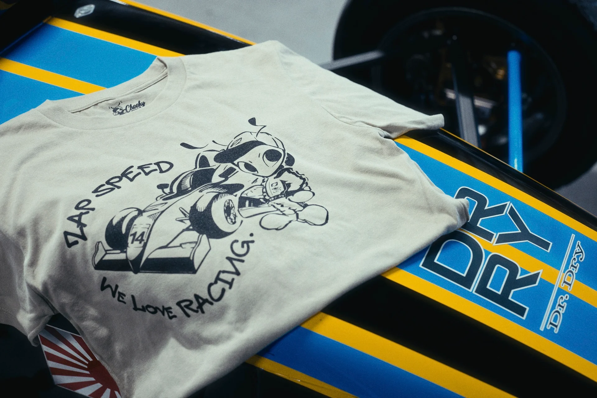 「ZAP SPEED WE LOVE RACING.」の文字とレーシングカーに乗るアリの絵を黒一色でスクリーンプリントした生成りのTシャツ
