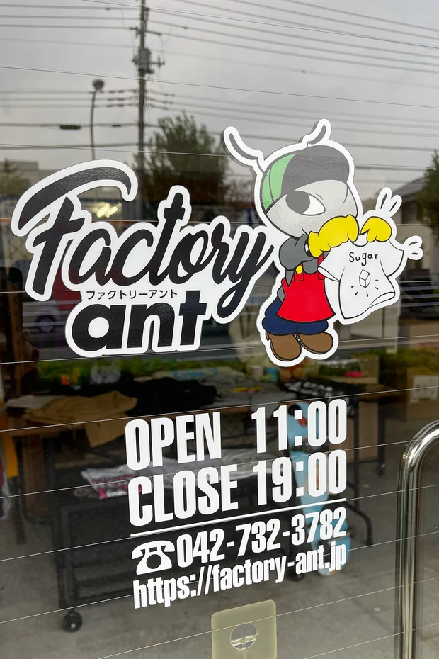 Factory antの入口のガラス。ロゴとアント君のステッカーの下に営業時間と電話番号のカッティングシート