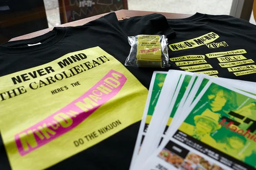 2025年に初めて開かれたニクオン町田BASEのイベントTシャツ。黒のTシャツに黄色とピンクでプリントし、背中には出演アーティストの名前